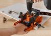 Blum ECODRILL jig used by Installer to drill hinge cup holes in a cabinet door. Quick-release clamp and integrated guides in use. Blum concealed hinges shown next to the workpiece.
