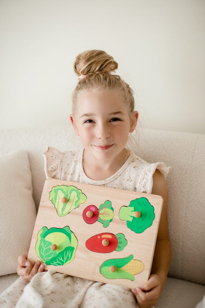 Child holding up a completed Qtoys Vegetable Knob Puzzle