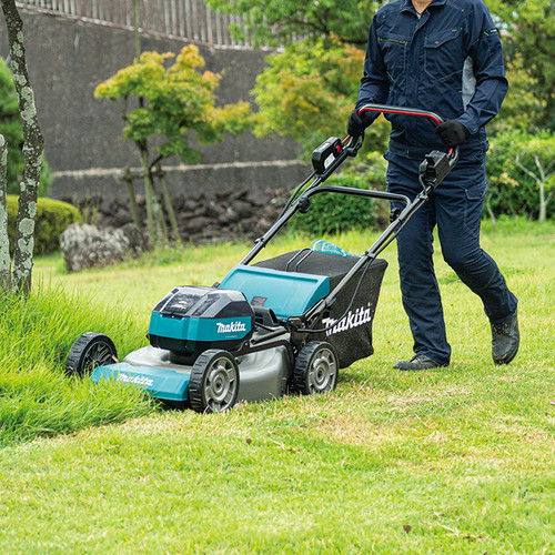 Person mowing a backyard lawn with a Makita cordless mower, wide lifestyle photo