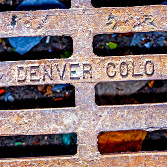 This image highlights the word Denver on a distressed city sewer wastewater grate.