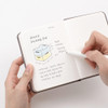 A person writing on fine grid pages in a Making Memory Mini planner, beside a colored storage box sketch and Korean notes.