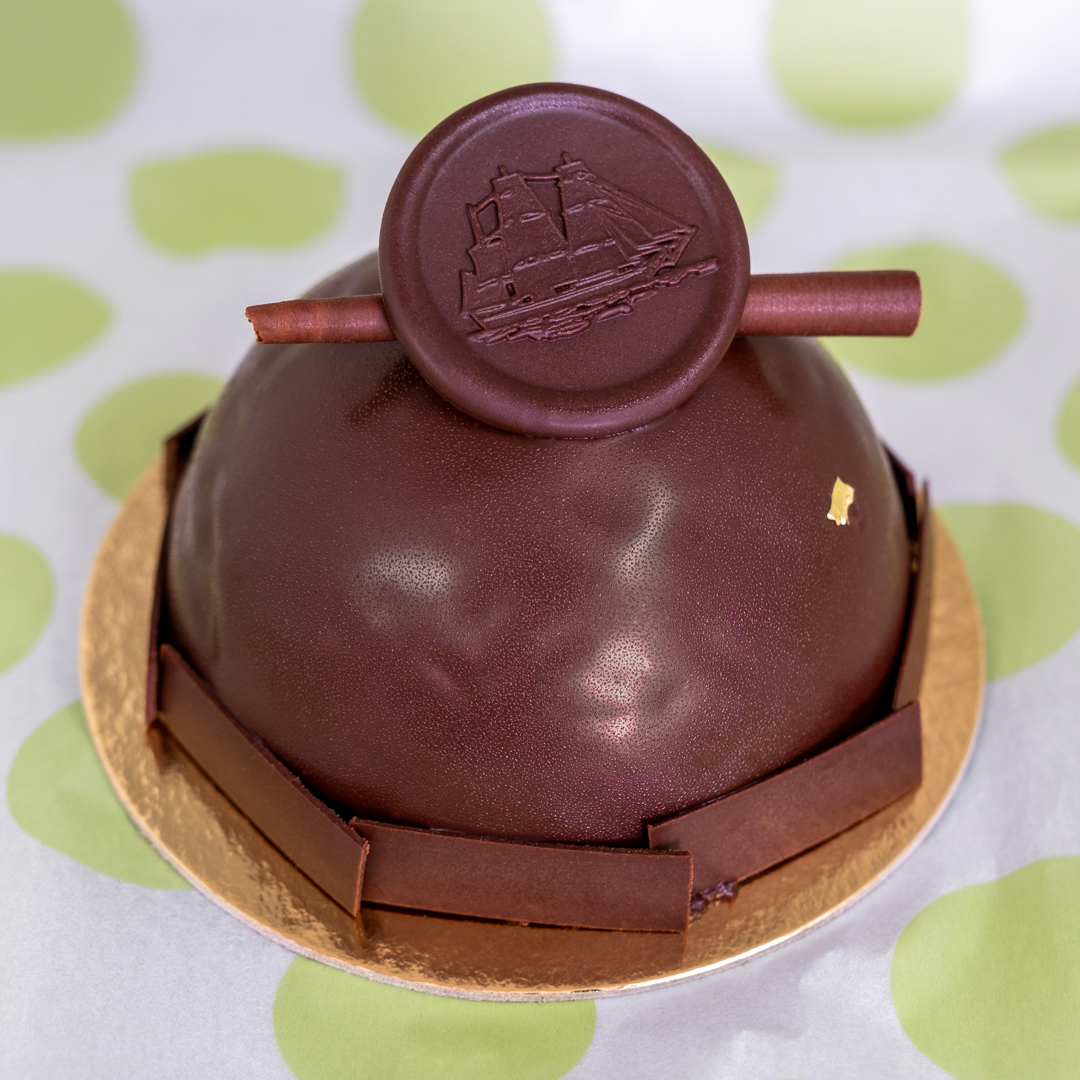 Chocolate Biscuit cake is topped with dark chocolate  mousse, a center of dark chocolate ganache,  brownie bits, covered in dark chocolate glaze  and dark chocolate garnish