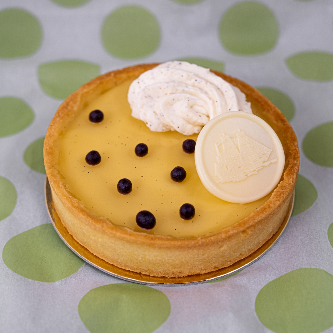 A buttery & tart passion fruit curd fills a vanilla shortbread tart shell. It is thinly glazed  with a passion fruit glaze