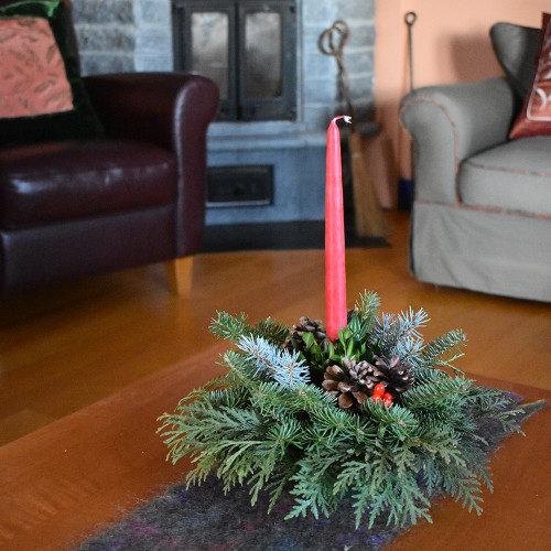 Tabletop centerpiece made with fresh greens and pinecones in a living room on coffee table. Red candle included.
