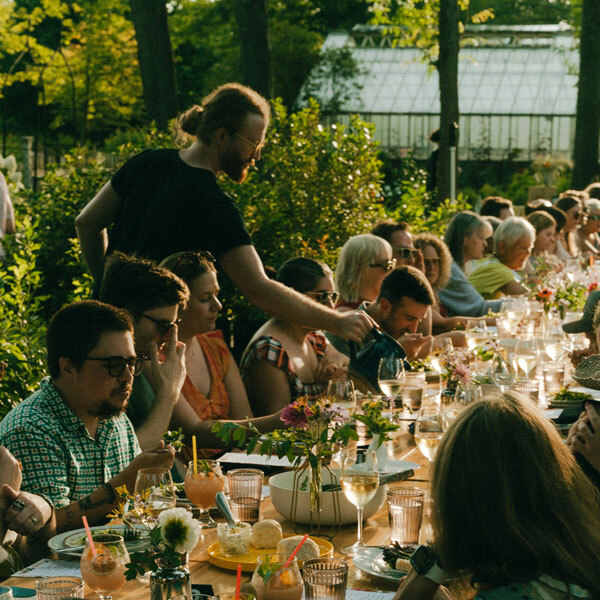 man serving water to a table of guests in a formal dining set up within a garden