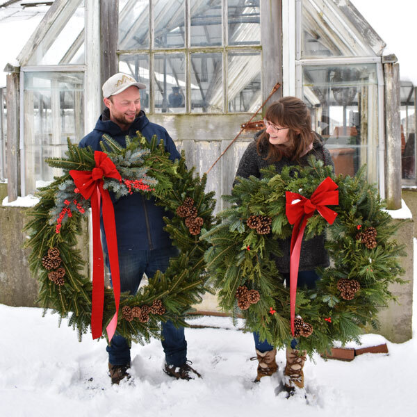 two people holding large wreaths in the snow in front of a greenhouse