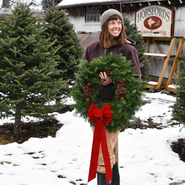 Woman holding wreath in front of trees with snow on the ground
