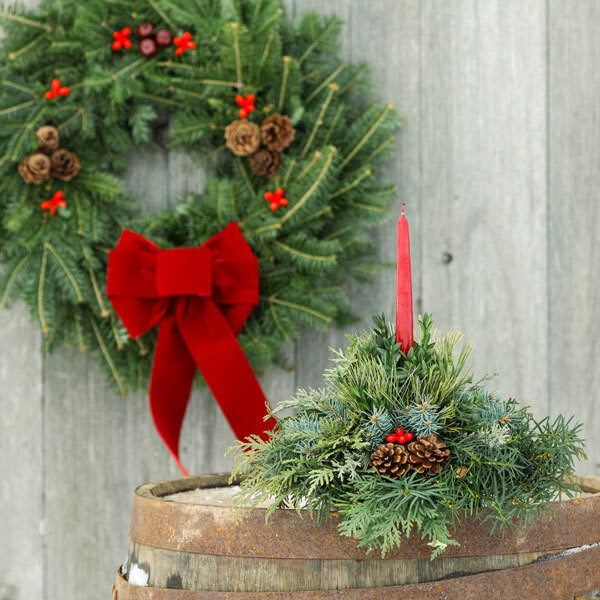 a centerpiece made of greens with a red candle in front of a blurred wreath