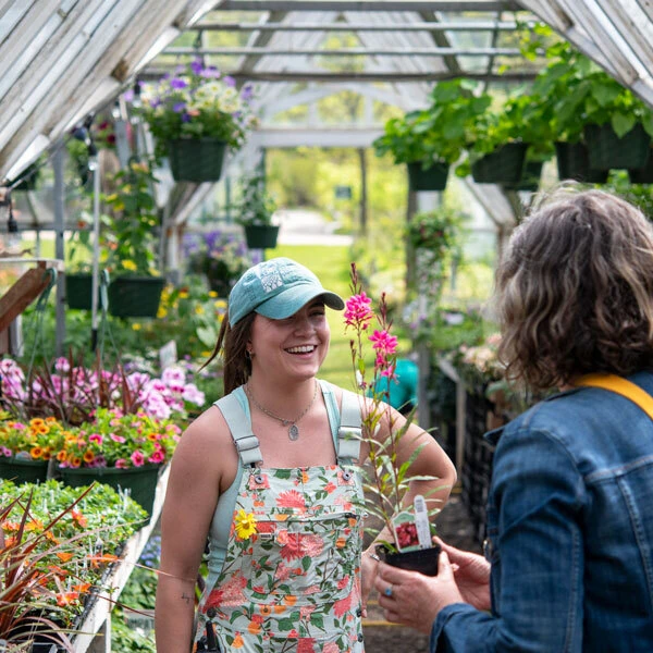 Woman in overalls smiling inside greenhouse