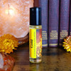 Shadow Scents Gold Perfume Oil - 1/3 oz. roll-on, yellow fragrance oil bottle with black cap on wooden surface, with books and flowers in the background.