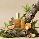 Kuumba Made Tunisian Patchouli Fragrance Oil - 1/2 oz., product image showing a bottle, roll-on, and a lid placed on a natural wood surface surrounded by ferns, orange slices, and pink flowers.