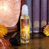 Shadow Scents Gold Perfume Oil - 1/3 oz. roll-on, a small transparent bottle with golden liquid, placed on a wooden surface with decorative salt lamps and yellow flowers in the background.