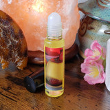 Shadow Scents Caramel Creme Perfume Oil - 1/3 oz. roll-on, a small transparent bottle with yellow fragrance oil and a rollerball applicator, placed on a wooden surface among decorative pottery and pink flowers.