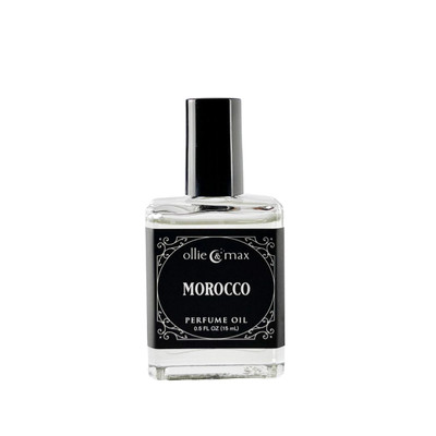 Ollie + Max Morocco Perfume Oil - 1/2 oz. , Clear glass bottle with black label and black cap, featuring elegant white decorative design and text.