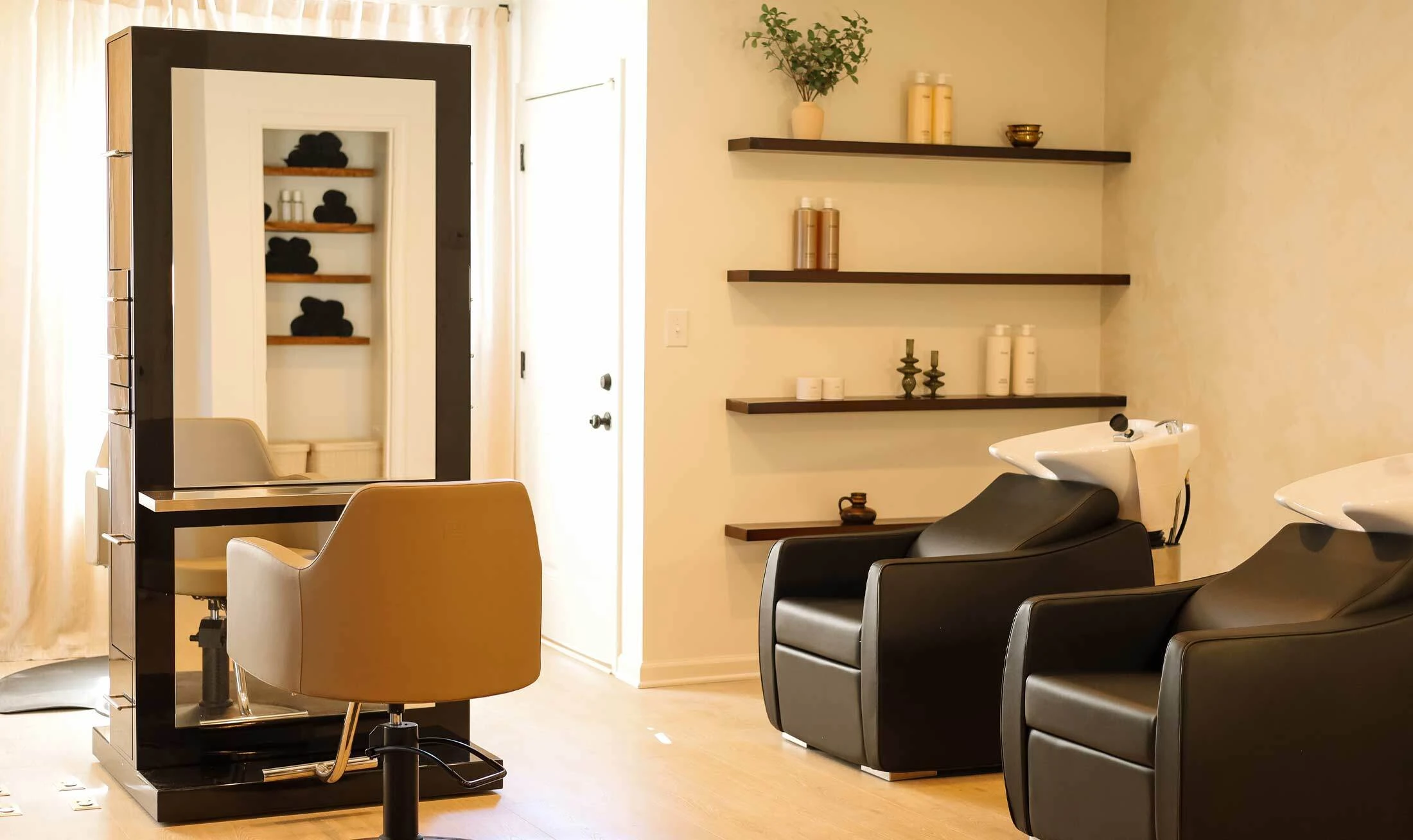 Black double sided styling station, beige salon styling chair, and two black shampoo systems with white bowls in a salon lifestyle setting