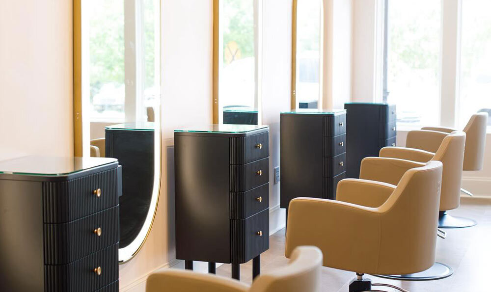 Row of black knoll styling stations, cashmere Venturi styling chairs, and gold Avalon LED mirrors
