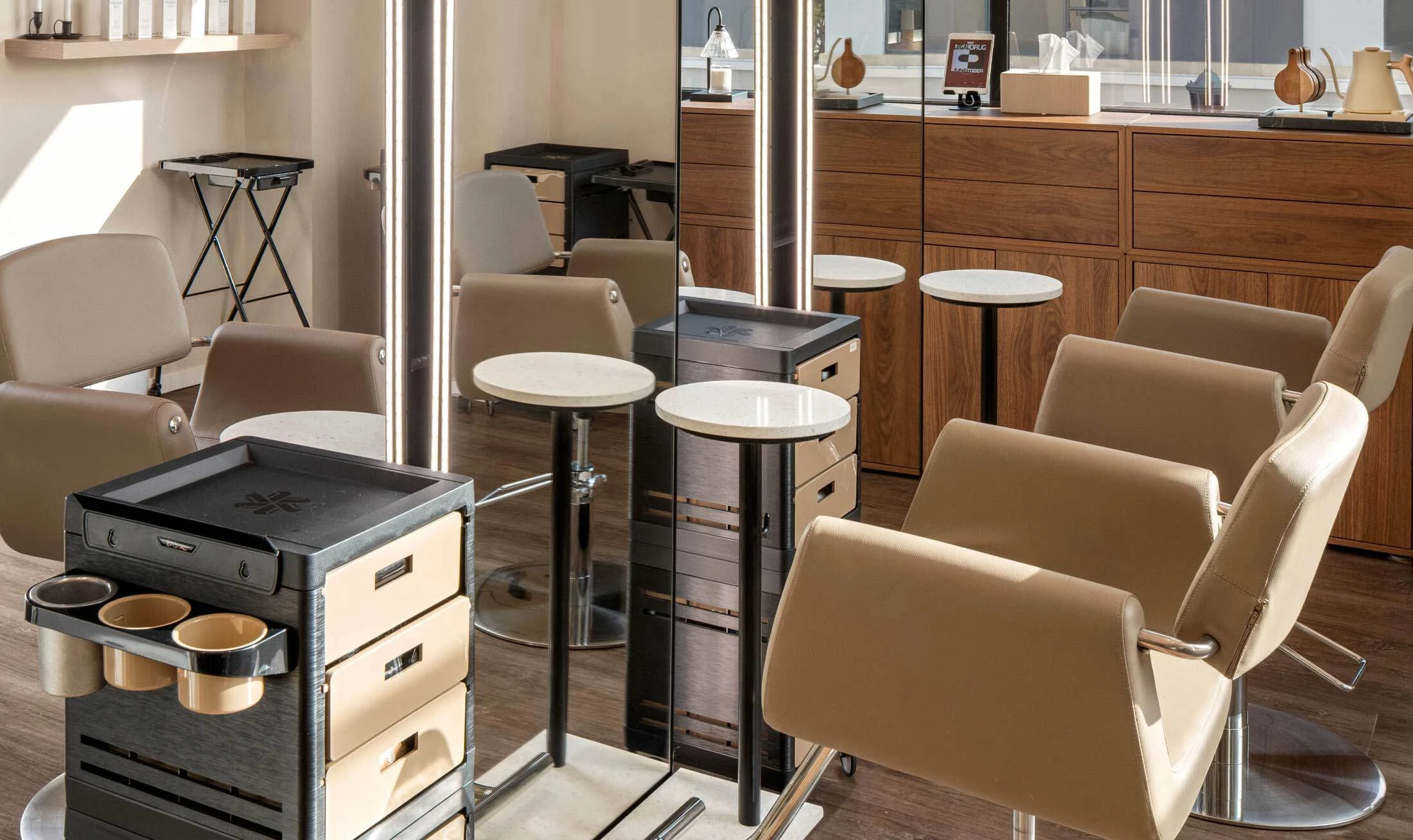 Black and beige mobile salon carts with color storage, appliance rings, and drawer storage next to LED salon mirrors and beige salon styling chairs in a salon