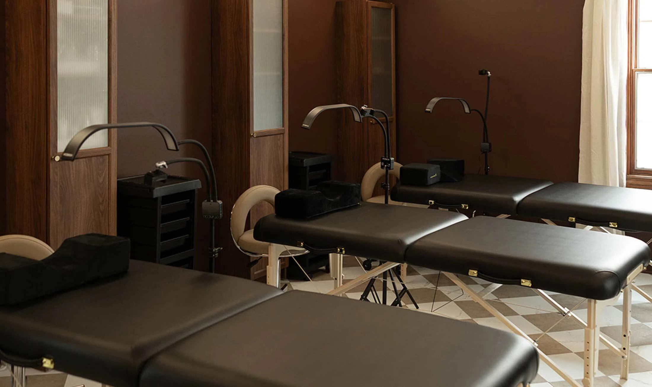 Spa and esthetician room showing line of black massage and facial tables with beige stools in a spa