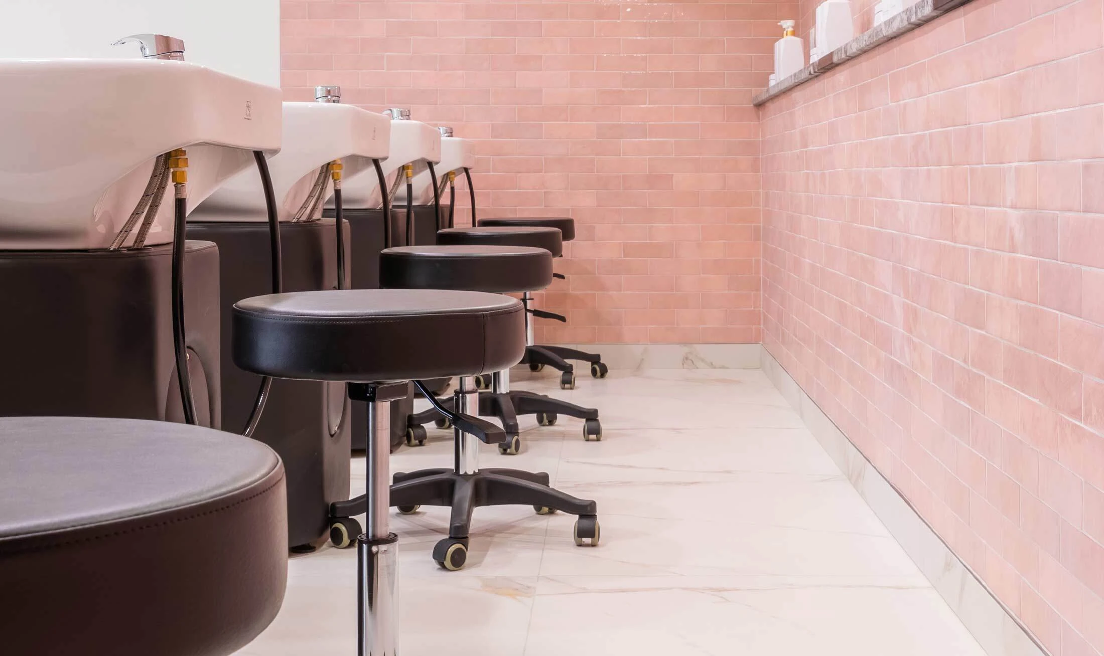 Lineup of black salon and spa tech stools in black behind a line of black shampoo systems in a salon