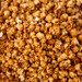 Close-up macro texture of handcrafted jumbo popcorn coated in rich copper-kettle caramel and dusted with genuine Old Bay seasoning.