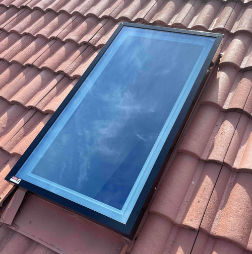 Solatube Premium Fixed Skylight with black frame installed on a terracotta tiled roof, reflecting blue sky.
