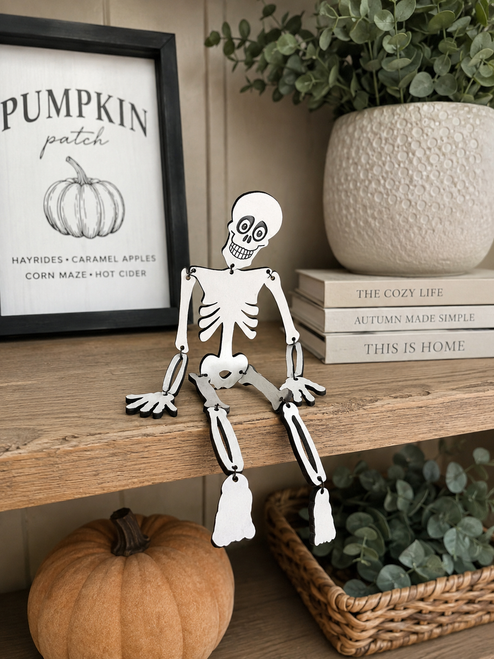 Cute wooden Halloween skeleton with movable arms and legs displayed on a rustic shelf with pumpkins and cozy fall farmhouse decor.