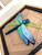 Dimensional 3D design adds depth and shadow, making the dragonfly appear as if it’s gently resting on the wood surface.