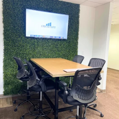 Standing-height conference table with ergonomic stools in front of a wall-mounted display in a Central Florida office