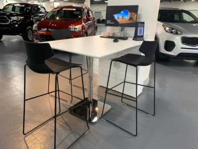 Showroom high-top table with black stools and a display screen next to new vehicles