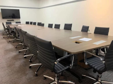 Large dealership conference table with black leather chairs and a wall-mounted TV