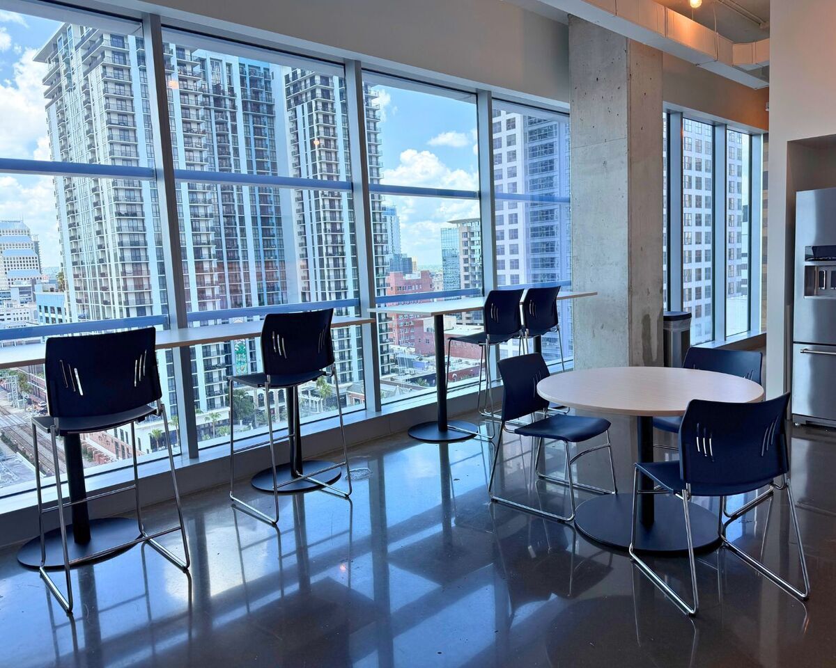 Break area with bar-height tables, navy stools, and round café table by city-view windows