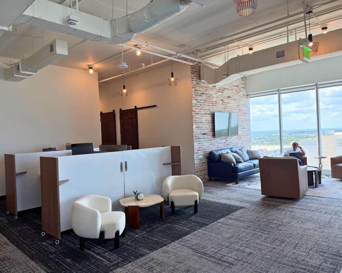 Open office with mobile workstation dividers, bouclé lounge chairs, and blue sofa beside brick accent wall