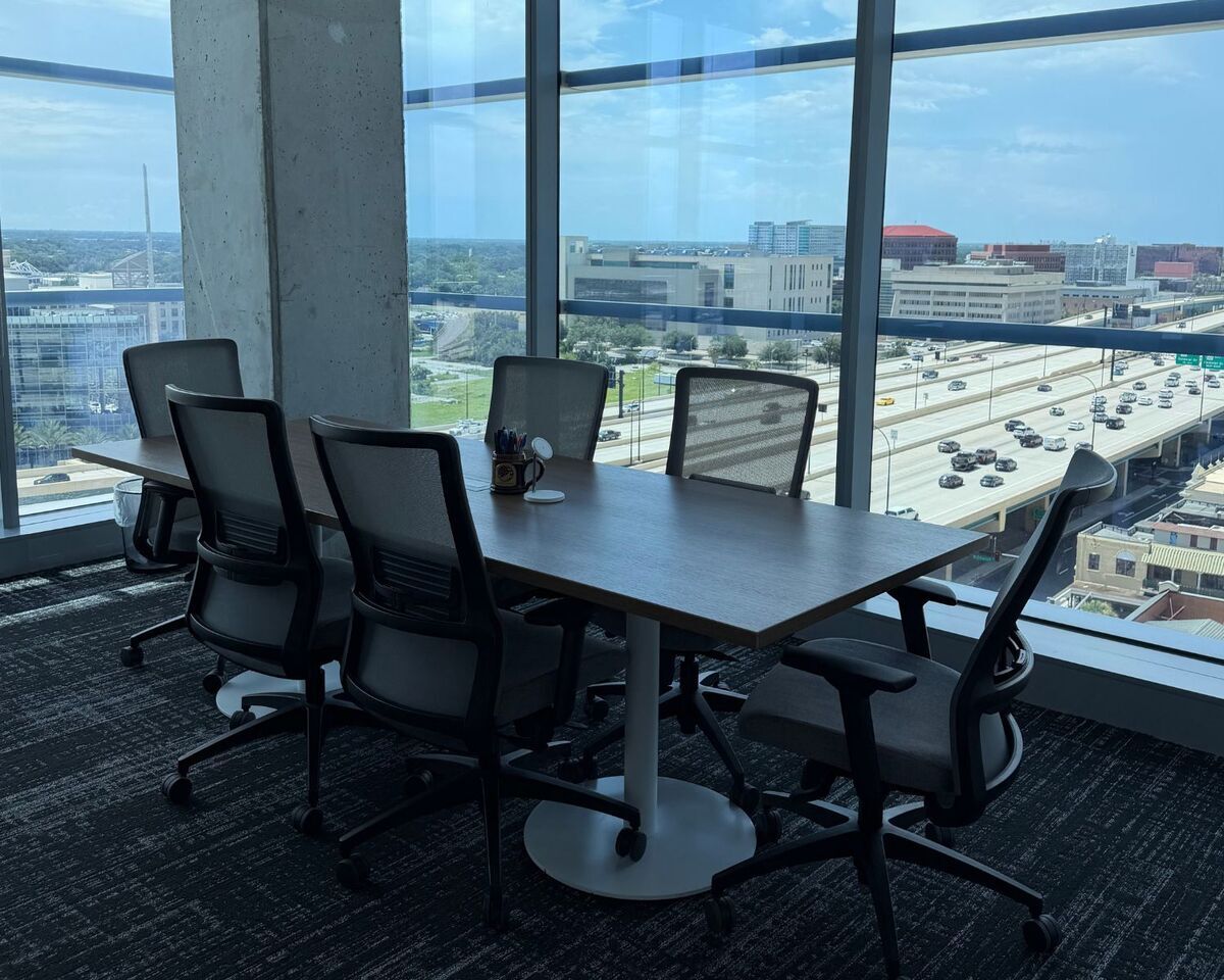 Window-side meeting table with black mesh task chairs overlooking Orlando skyline