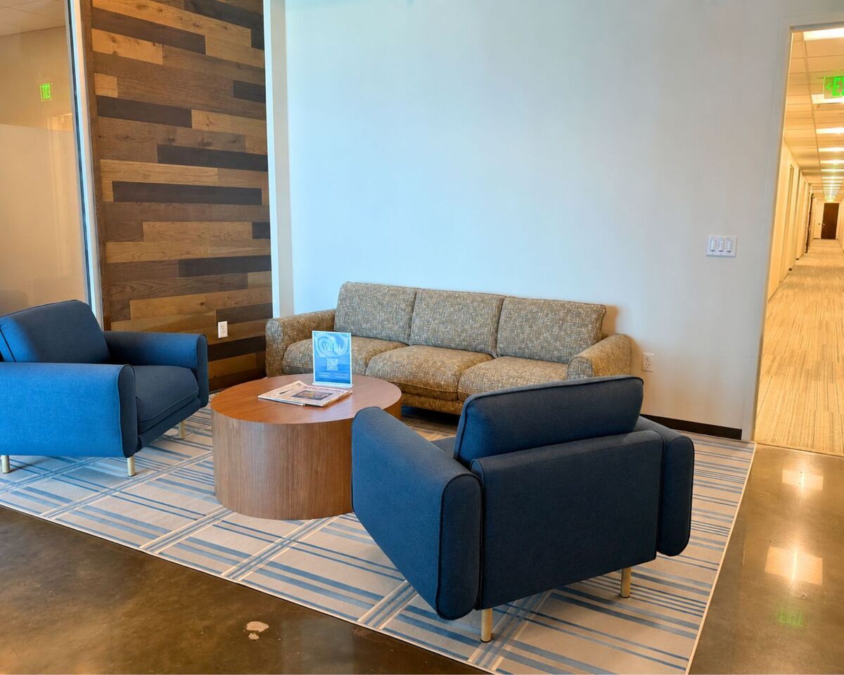 Reception seating area with blue armchairs, tweed sofa, and round wood coffee table