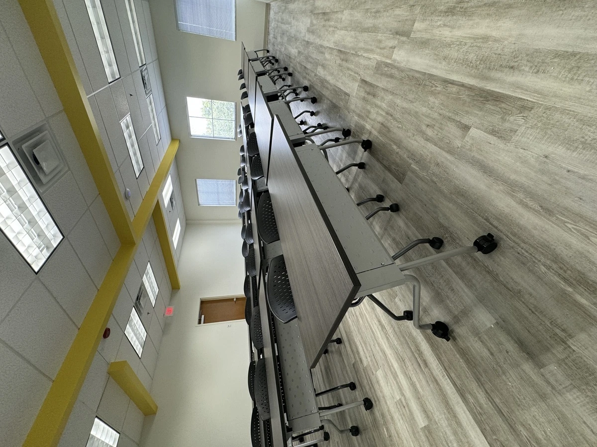 Rows of mobile training tables and perforated-back chairs under yellow ceiling beams