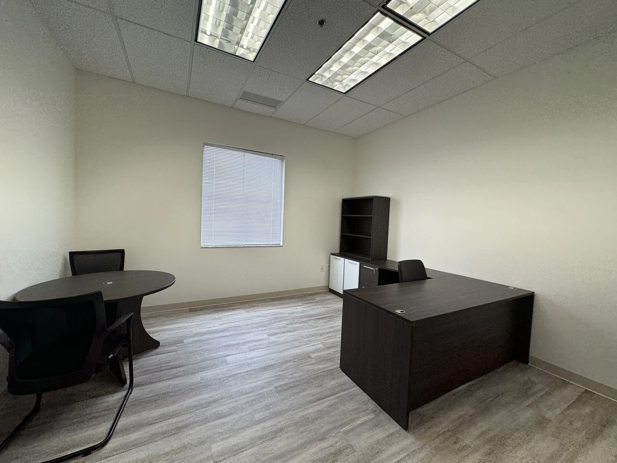 Private office with round conference table, guest chairs, and L-shaped workstation