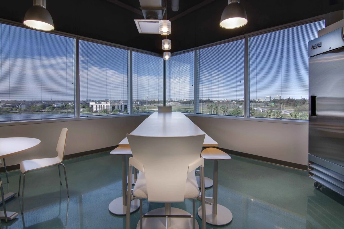Corner break space with long white high-top table, stools, and city-view windows