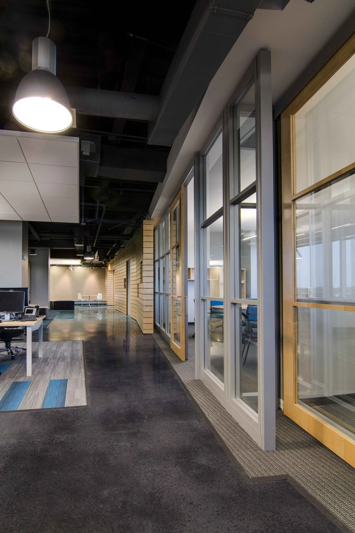 Office corridor with glass-front meeting rooms, wood-framed doors, and workstation desks