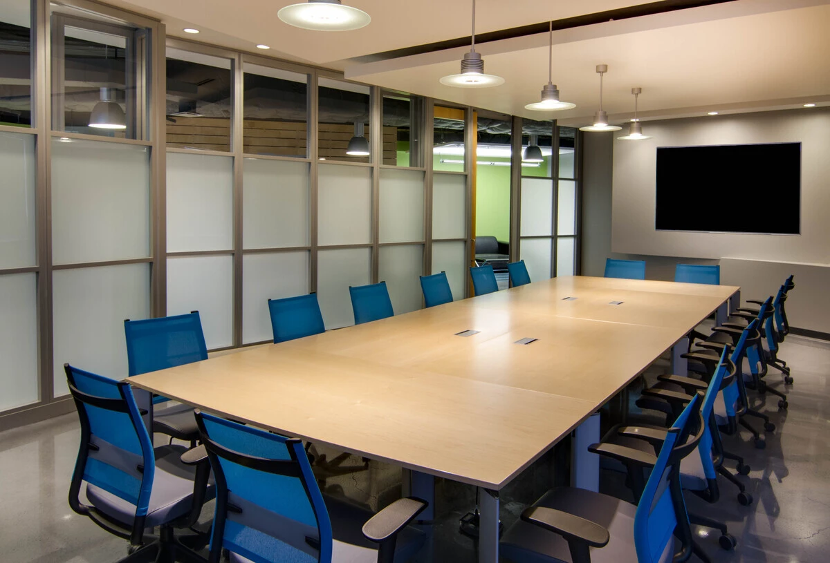 Boardroom with maple conference table, blue mesh chairs, and frosted glass wall