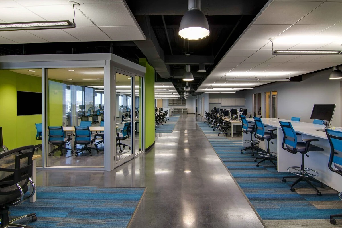 Open office with bench-style white tables, blue drafting stools, and task seating
