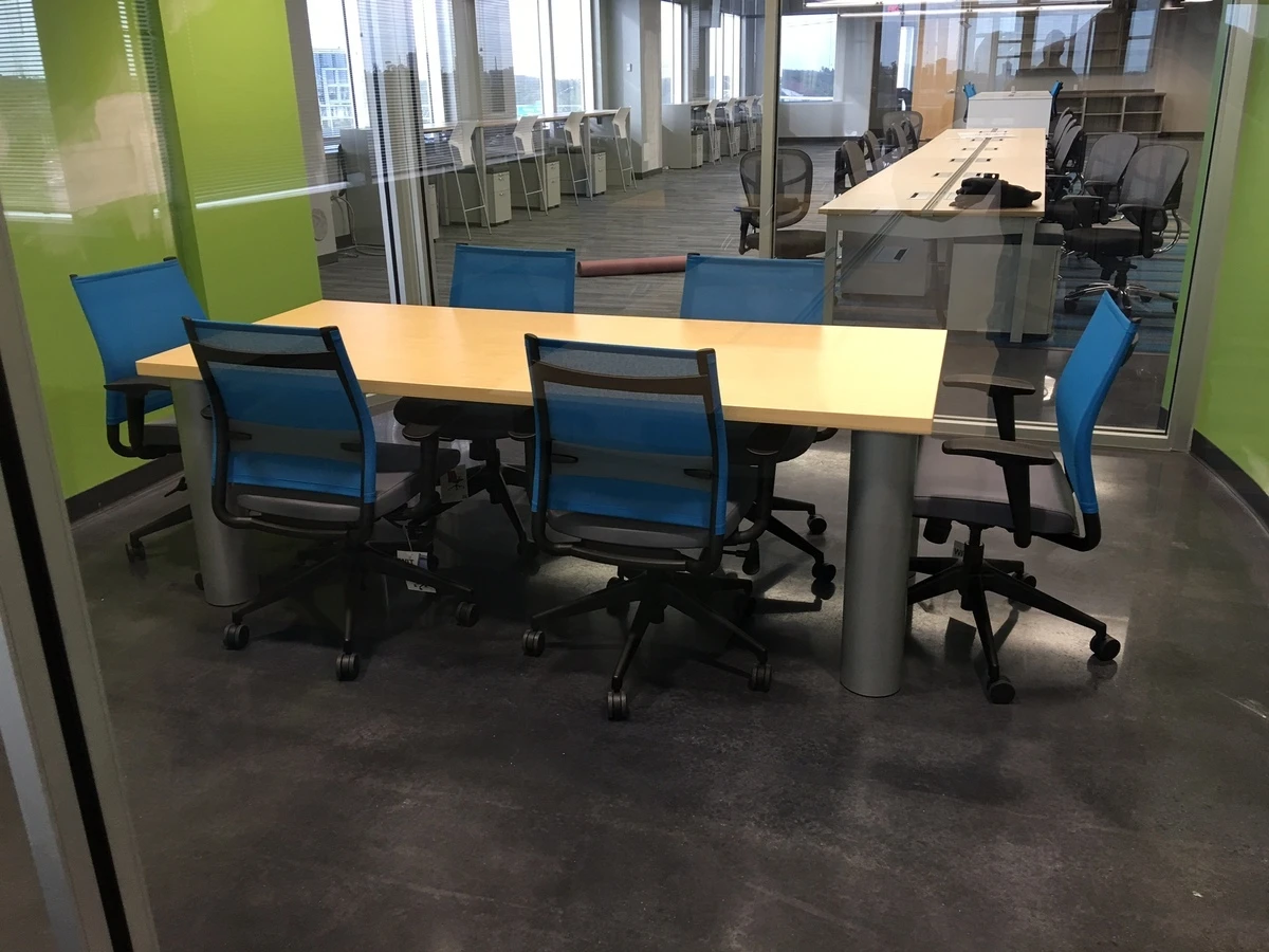Glass-enclosed meeting room with wood-top table and blue mesh task chairs