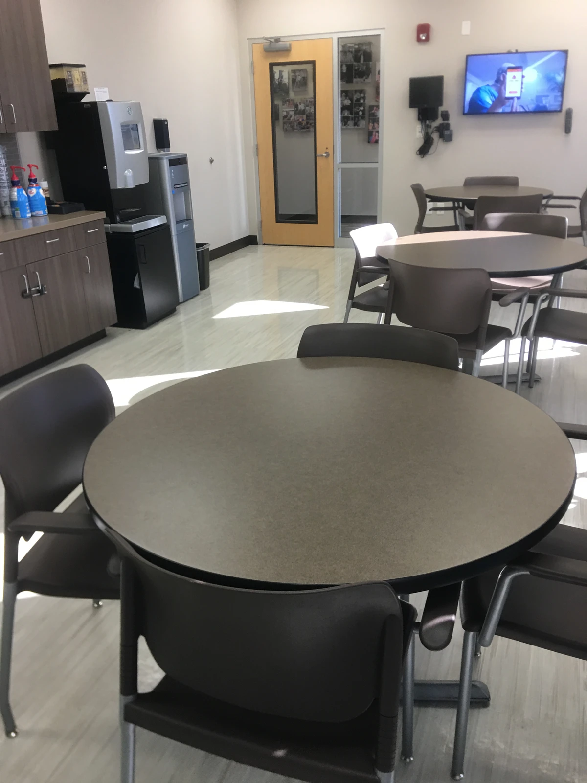Break room with round tables, arm chairs, coffee station, and wall-mounted display