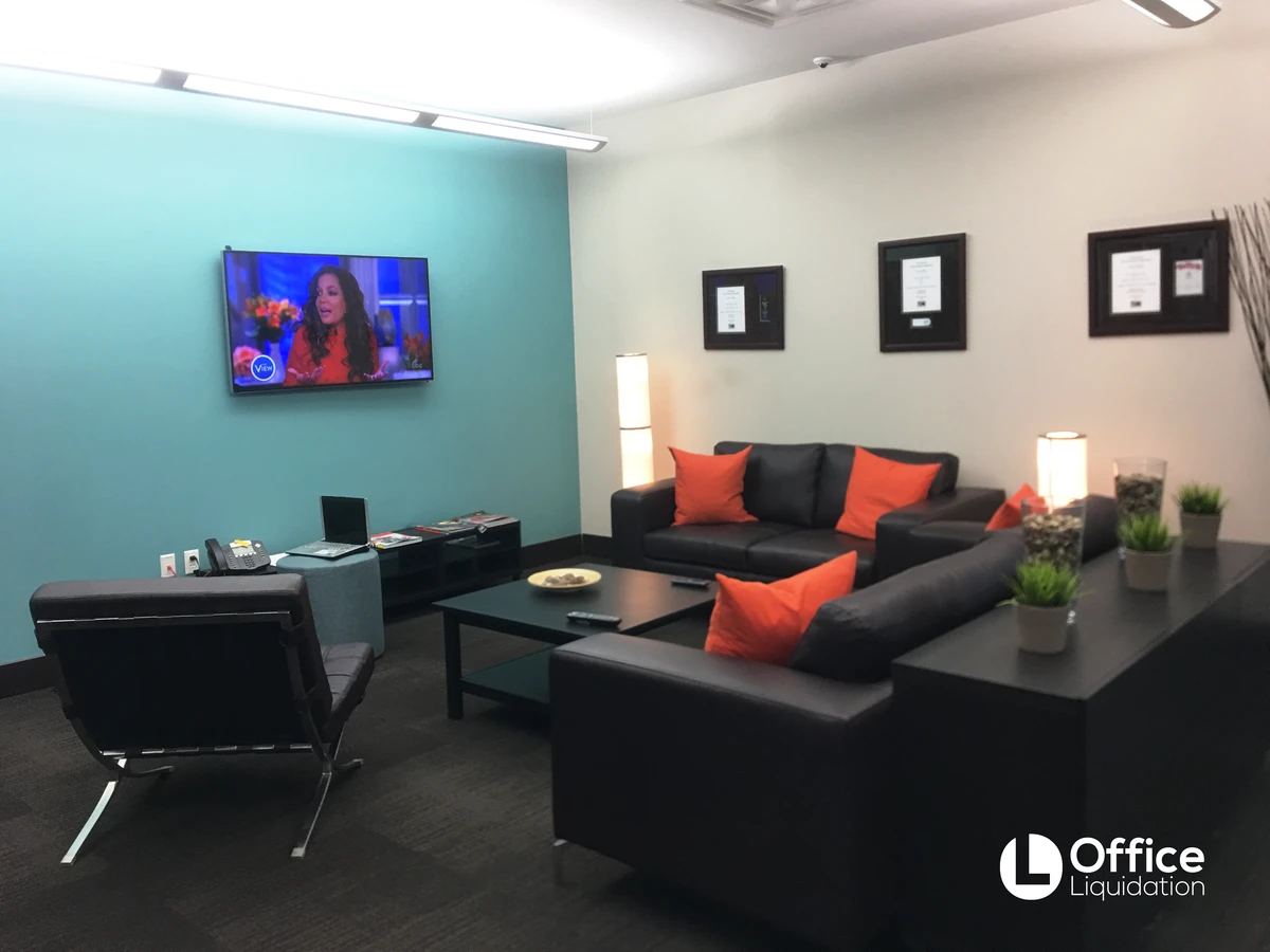 Lounge with black leather sofas, orange accent pillows, wall-mounted TV, and teal accent wall
