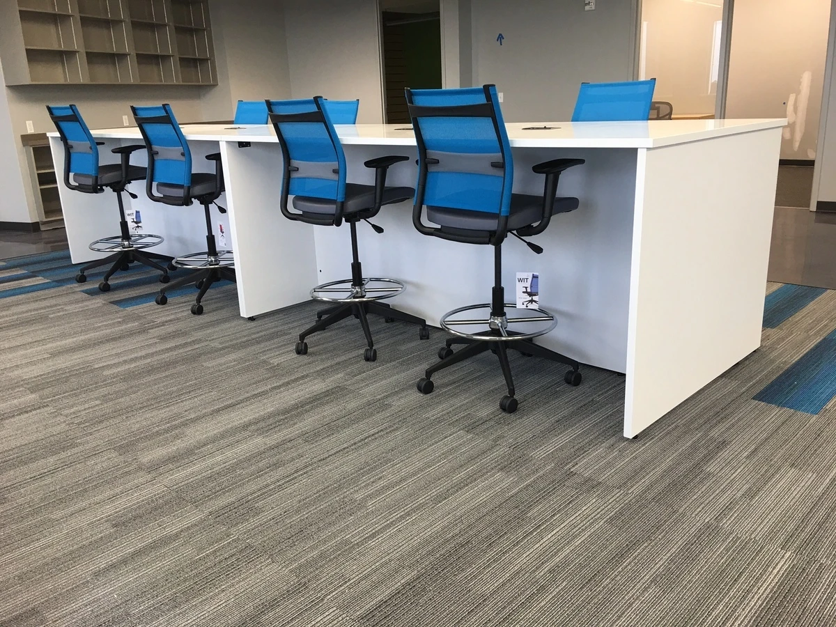 White collaboration table with blue mesh drafting stools and foot rings