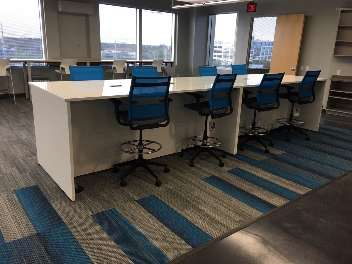Standing-height collaboration table with blue mesh stools and bar seating by windows
