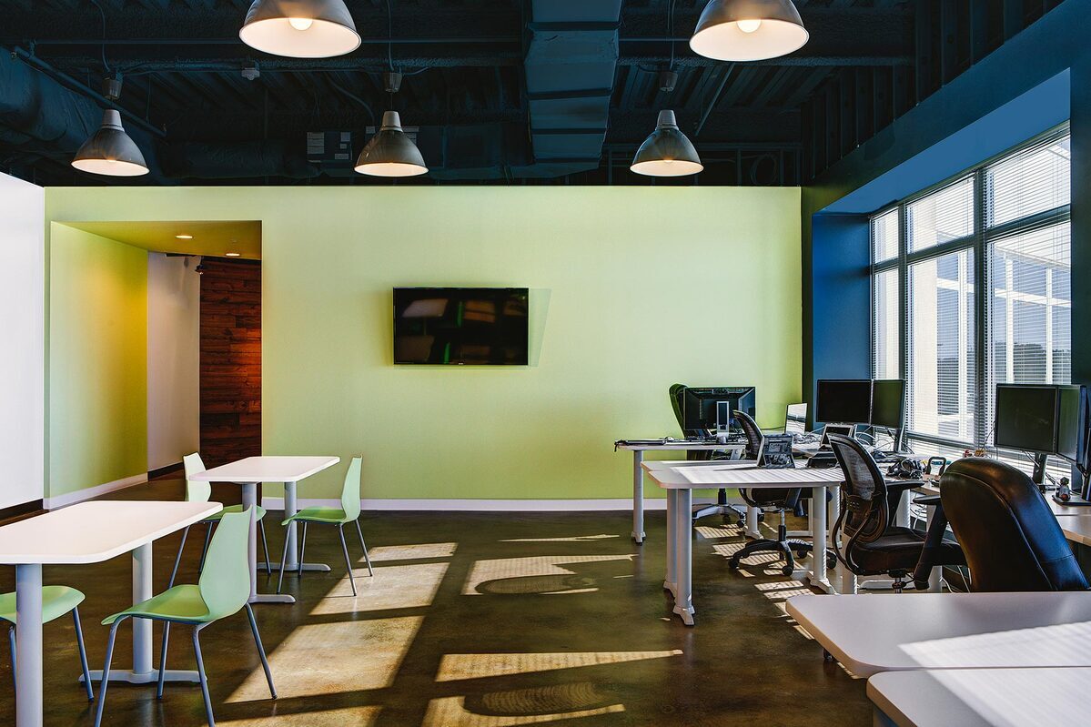 Collaborative seating area with white tables and green chairs next to desks with monitors