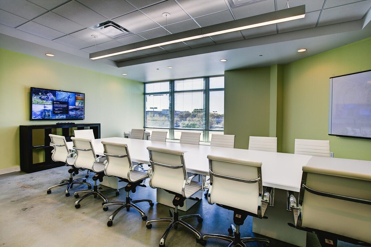 Conference room with white table, ribbed white chairs, wall display, and whiteboard