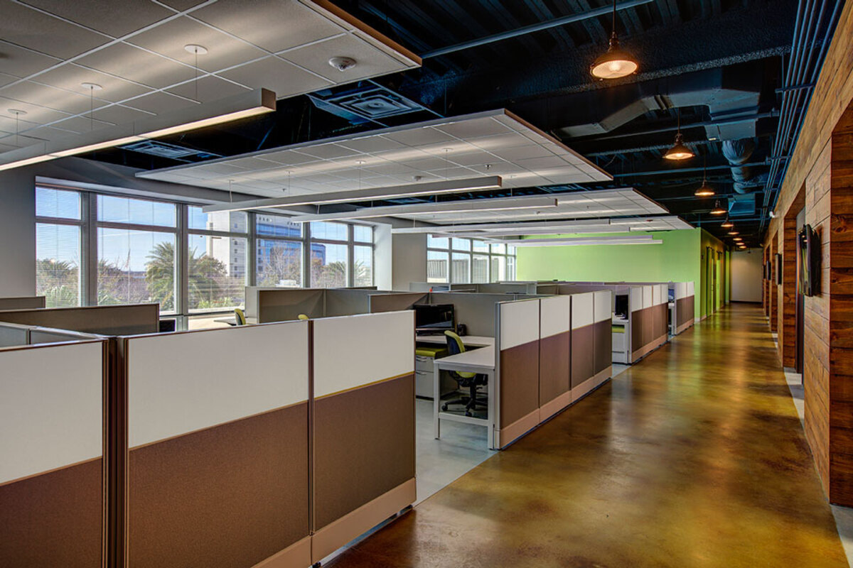 Row of cubicle workstations beside a wood-paneled wall and stained concrete floor