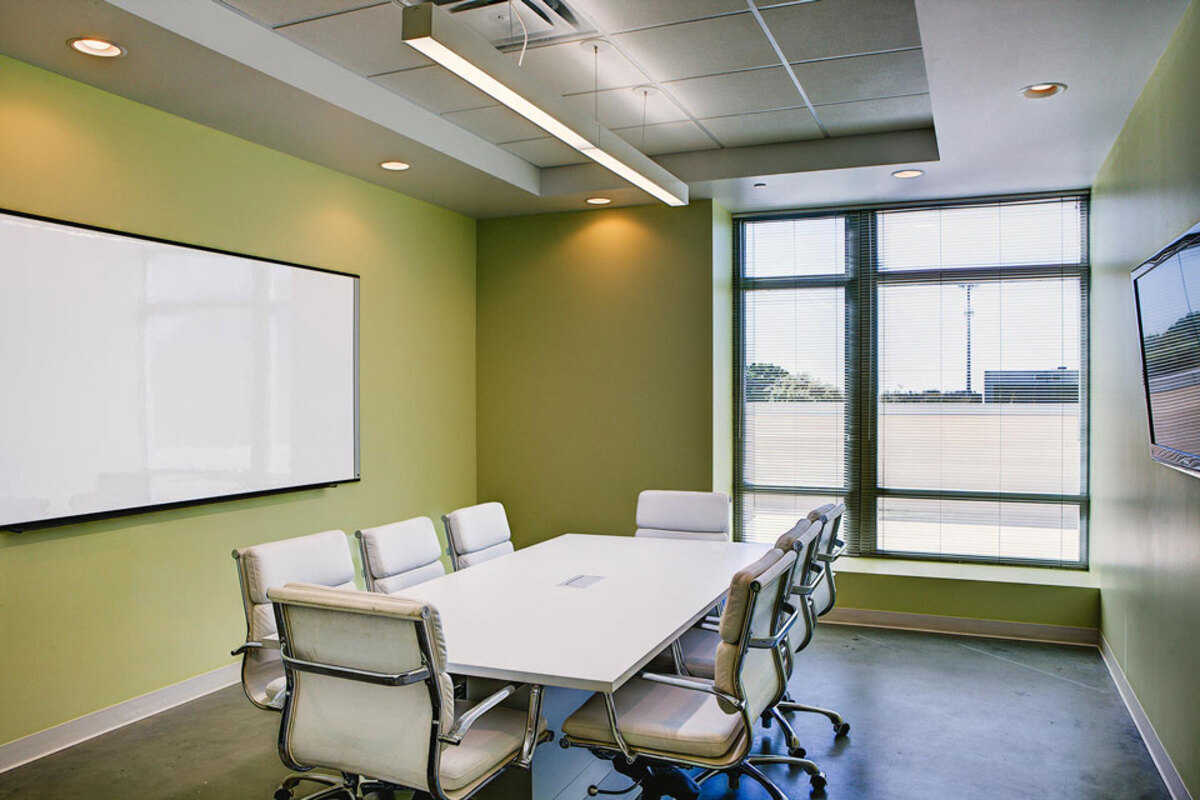 Small conference room with white table, ribbed white chairs, whiteboard, and wall-mounted display