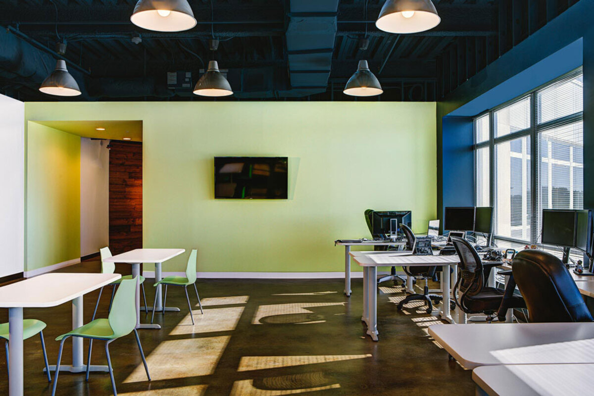 Flexible work area with white café tables, green shell chairs, and desks with mesh task chairs